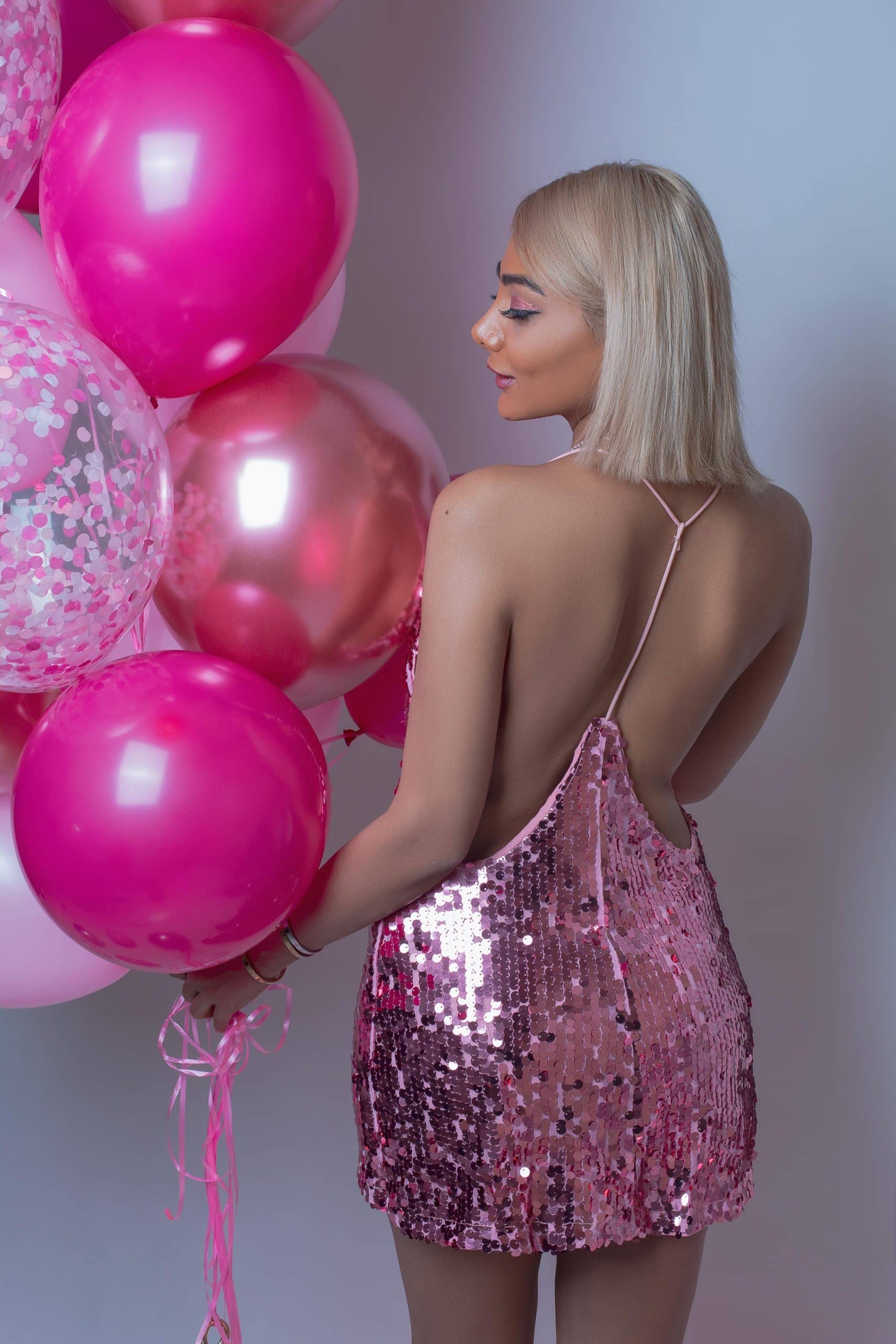 Female Model in pink sparkly dress holding a Custom balloon décor bouquet of pink helium balloons speckled and transparent